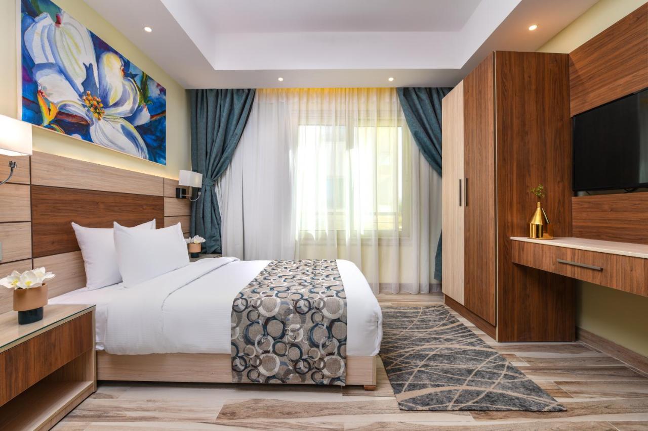 Tolip Resort El Galala Majestic Ajn Suchna Zewnętrze zdjęcie The photo shows a well-designed hotel room. It features a comfortable bed with a decorative bedspread and two pillows. There are soft curtains framing a window that lets in natural light. On one side, there is a colorful piece of artwork hanging on t