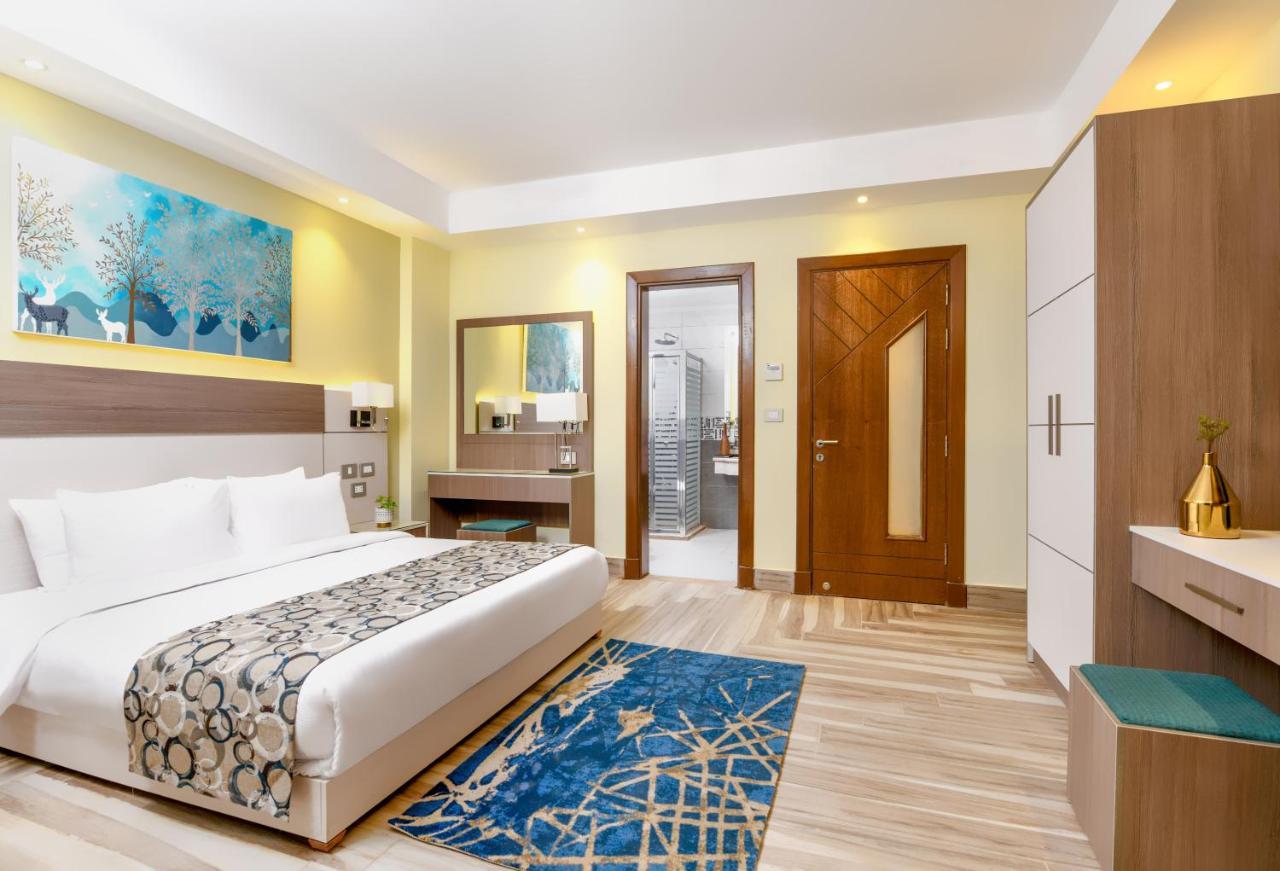 Tolip Resort El Galala Majestic Ajn Suchna Zewnętrze zdjęcie The photo shows a well-decorated hotel room. There is a large bed with white linens and a decorative throw blanket. The room features a wooden wardrobe and a bedside table with lamps. A colorful rug is placed on the floor, adding warmth to the space.