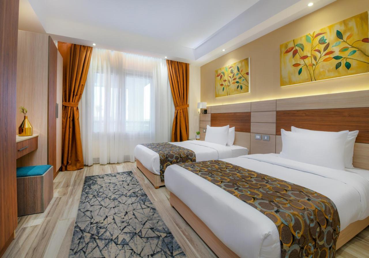 Tolip Resort El Galala Majestic Ajn Suchna Zewnętrze zdjęcie The photo shows a modern hotel room with two single beds, each covered with white linens and decorative brown bed throws. The walls are painted in warm colors, and there are two pieces of artwork featuring floral and leaf designs above the beds. The 