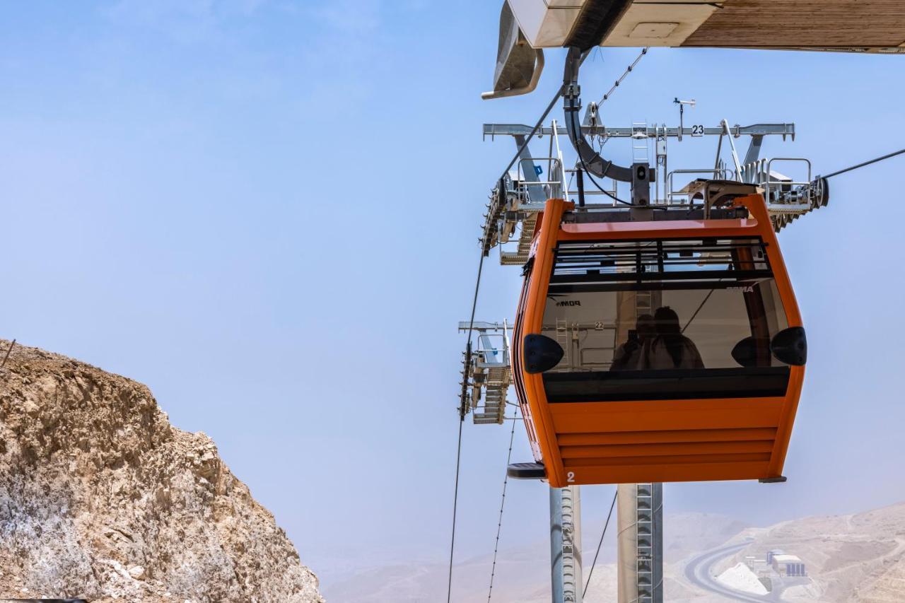 Tolip Resort El Galala Majestic Ajn Suchna Zewnętrze zdjęcie The photo shows an orange gondola or cable car hanging on a cable system. The gondola appears to be suspended in the air above a rocky landscape, with a clear sky in the background. There are supporting cables and structures visible, indicating that 