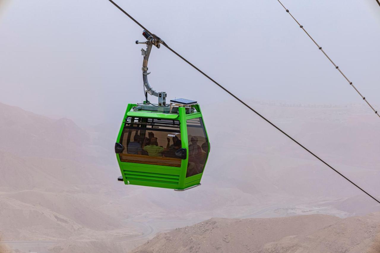 Tolip Resort El Galala Majestic Ajn Suchna Zewnętrze zdjęcie The photo shows a green cable car suspended in the air, moving along a wire. The cable car appears to be traversing a mountainous landscape, which looks rocky and arid. The surrounding environment is somewhat foggy or hazy, suggesting limited visibil