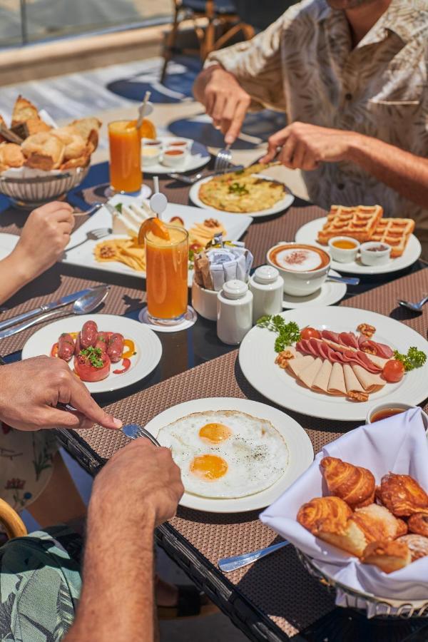 Tolip Resort El Galala Majestic Ajn Suchna Zewnętrze zdjęcie The photo features a spread of breakfast dishes on a table. There are two sunny-side-up eggs on one plate, surrounded by various food items, including slices of ham, sausages, and fresh tomatoes. Another plate holds a serving of waffles. A bowl with 