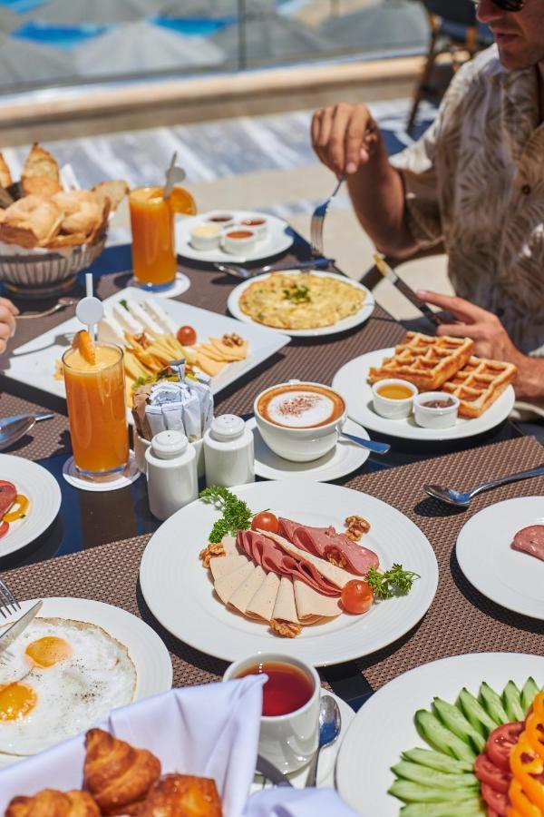 Tolip Resort El Galala Majestic Ajn Suchna Zewnętrze zdjęcie The photo shows a breakfast spread laid out on a table. There are several plates with a variety of food items, including:

1. **Sliced Cold Cuts**: A plate featuring various cold meats, accompanied by garnishes like cherry tomatoes and lettuce.
2. **