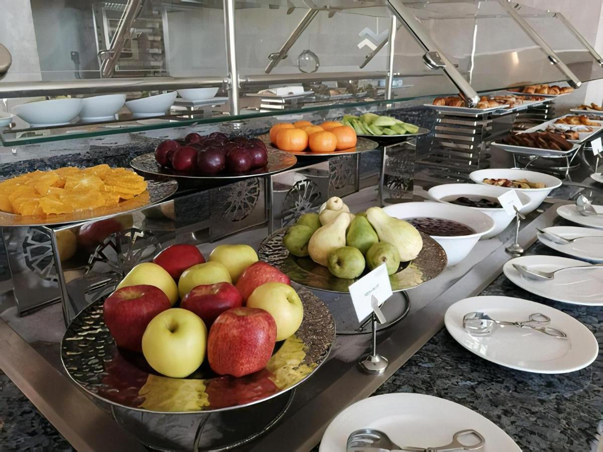 Tolip Resort El Galala Majestic Ajn Suchna Zewnętrze zdjęcie The photo displays a buffet setup featuring an assortment of fresh fruits arranged on several tiered trays. There are red and green apples, pears, grapes, and oranges. Adjacent to the fruit display, there are several bowls containing various other fo