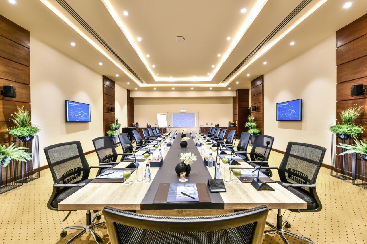 Tolip Resort El Galala Majestic Ajn Suchna Zewnętrze zdjęcie The photo shows a modern conference room designed for meetings. It features a long rectangular table at the center, surrounded by ergonomic black chairs. The room is well-lit with ceiling lights and has a neutral color scheme. There are two large scr