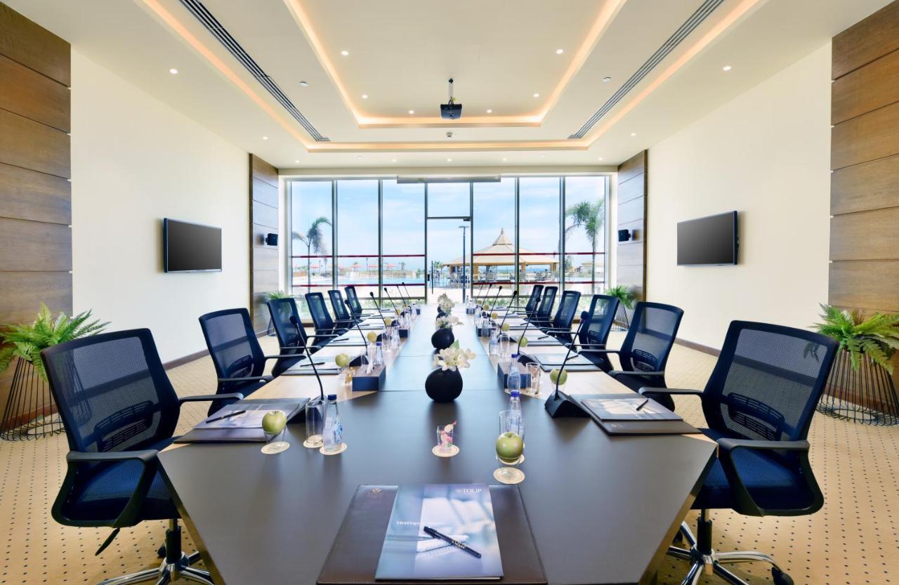Tolip Resort El Galala Majestic Ajn Suchna Zewnętrze zdjęcie The image shows a modern conference room with a large, dark rectangular table surrounded by ergonomic black chairs. The room features large windows that allow natural light to enter and provide a view of the outdoors, including some greenery. On the 