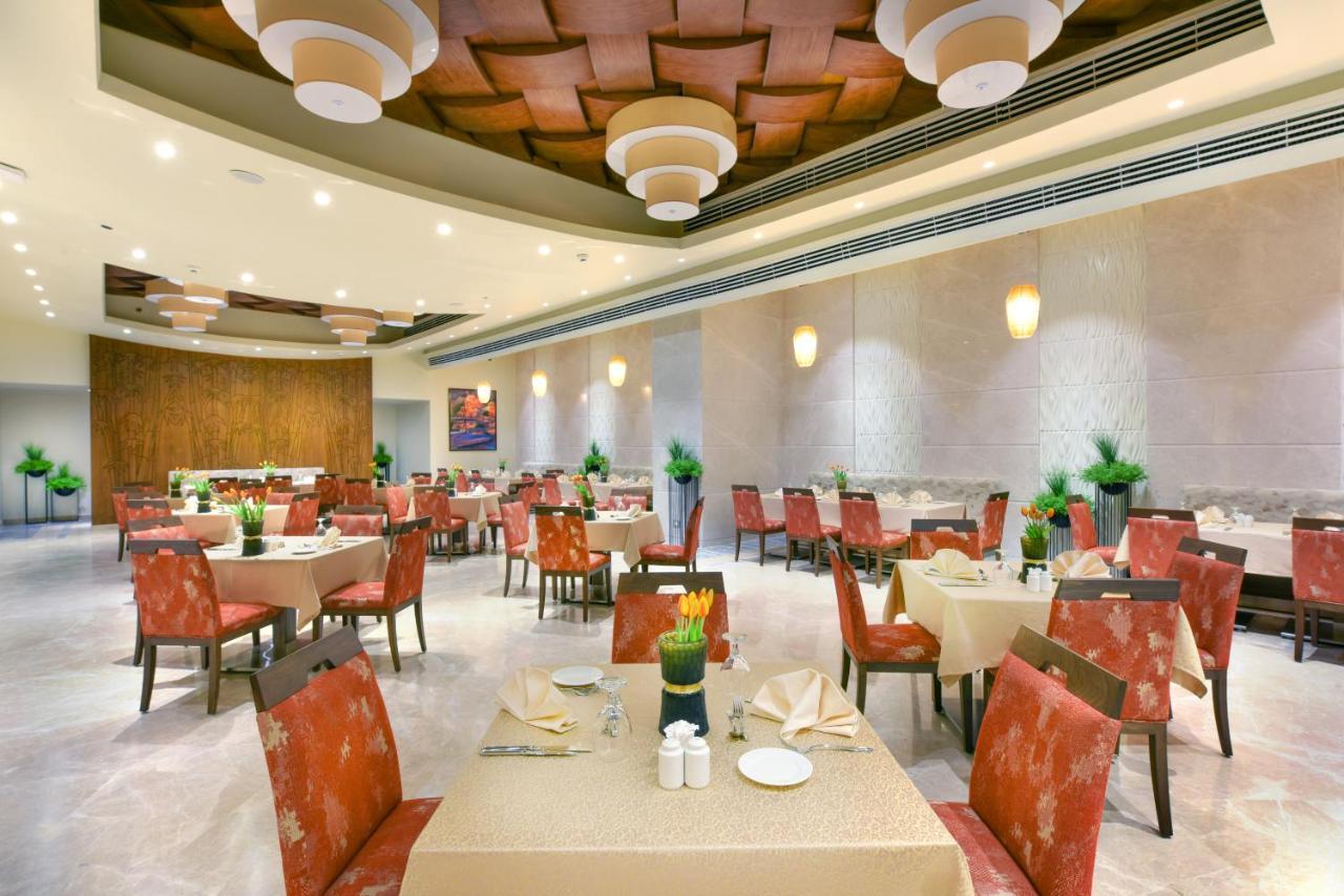 Tolip Resort El Galala Majestic Ajn Suchna Zewnętrze zdjęcie The photo shows the interior of a restaurant. The space features several tables set with light-colored tablecloths and chairs with reddish upholstery. Each table is adorned with decorative napkins and has small plants in the center. The room has a mo