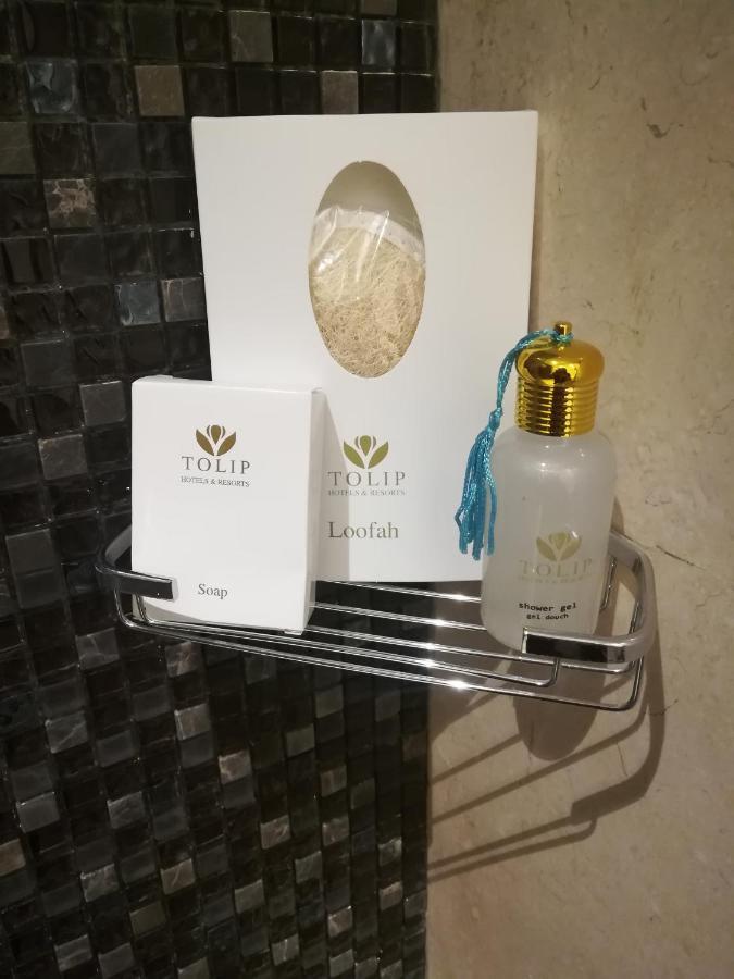 Tolip Resort El Galala Majestic Ajn Suchna Zewnętrze zdjęcie The photo shows a small metal shelf containing three items related to personal care. 

1. **Soap**: A white box labeled "TOLIP" with the word "Soap" visible on the front.
2. **Loofah**: A package with the same "TOLIP" branding, containing loofah.
3. 
