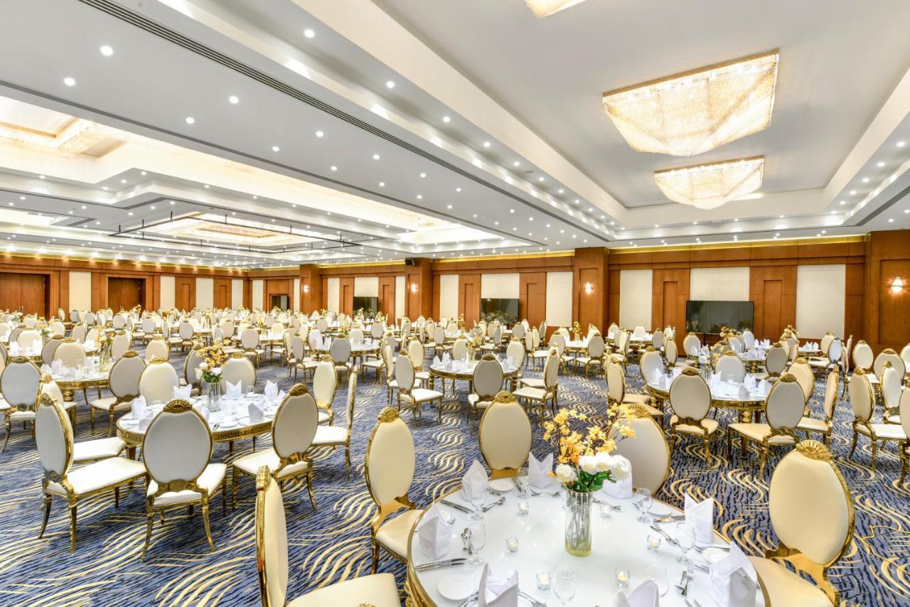 Tolip Resort El Galala Majestic Ajn Suchna Zewnętrze zdjęcie The photo shows a spacious and elegantly decorated banquet hall. The room features numerous round dining tables, each set with white tablecloths and adorned with decorative centerpieces, likely flowers. The chairs surrounding the tables have a luxuri